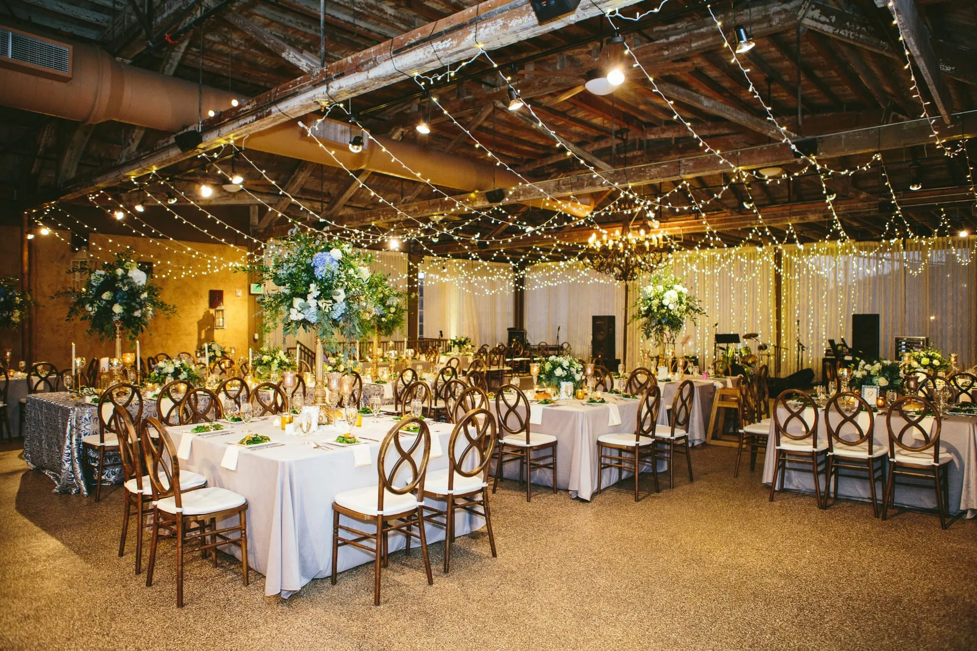 Long tables under a canopy of warm string lights, the timber roof structure lit above them