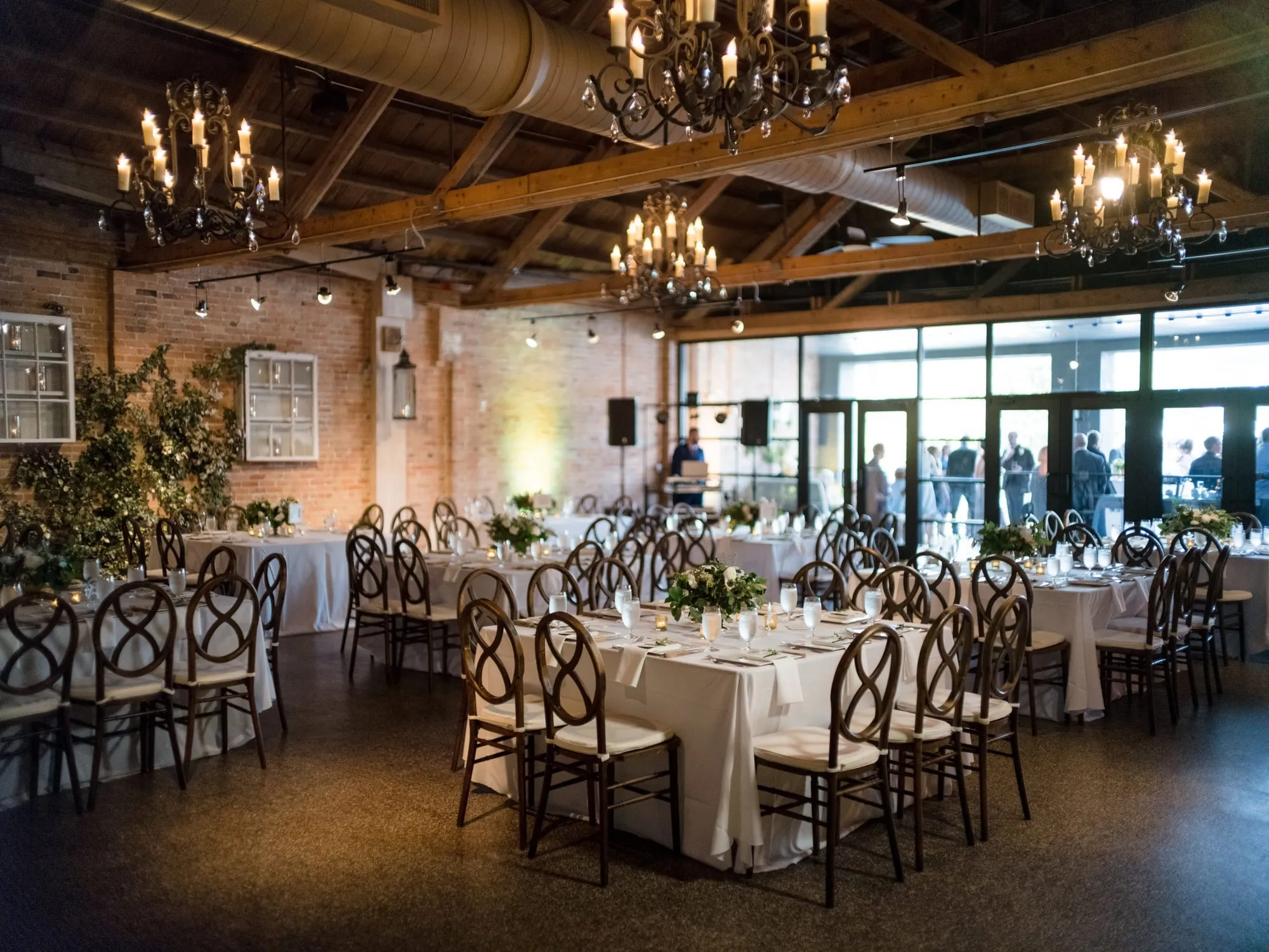 Daylight through the windows, chandeliers above round and long tables set in white