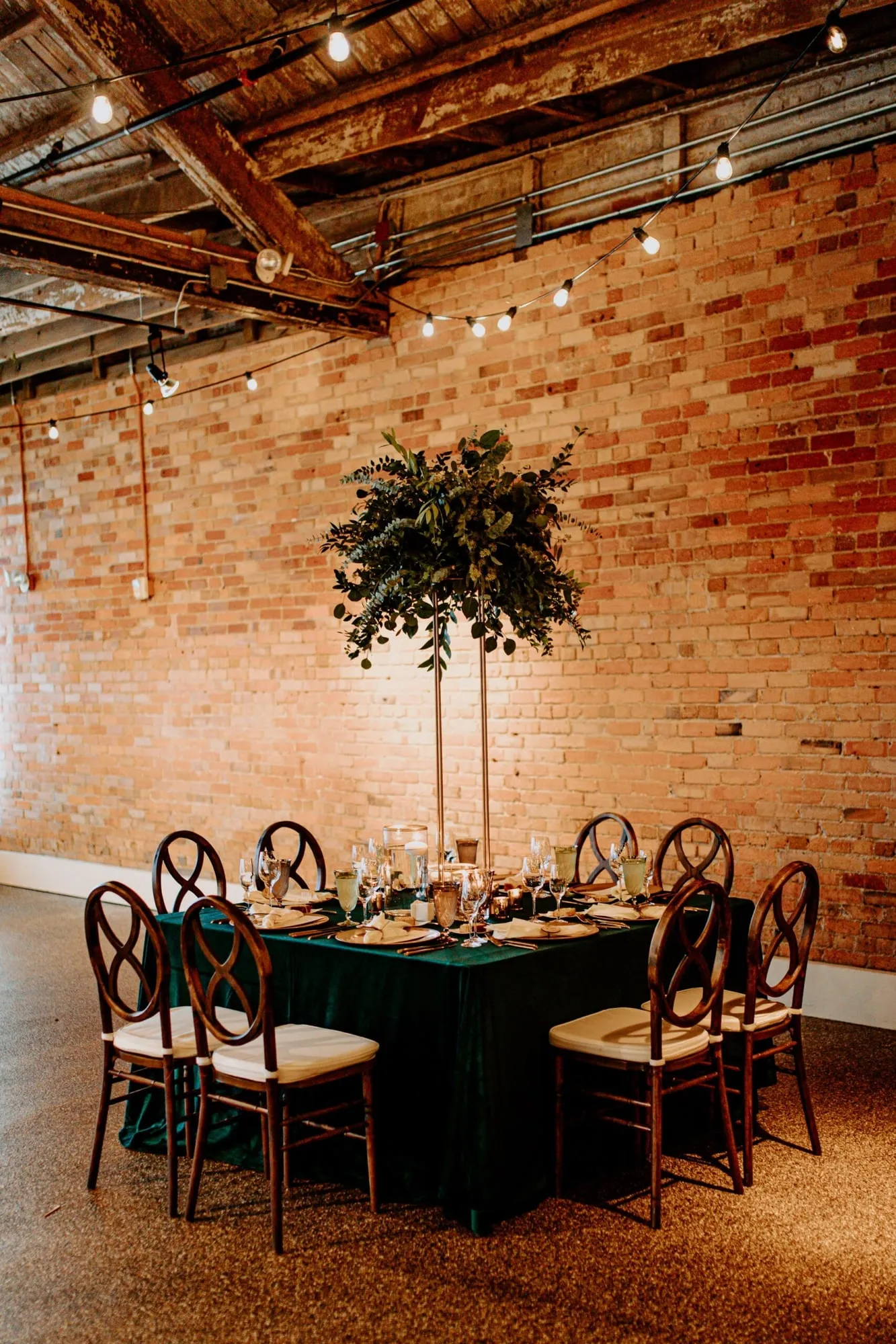 A single round table against bare brick, a small tree standing at its center