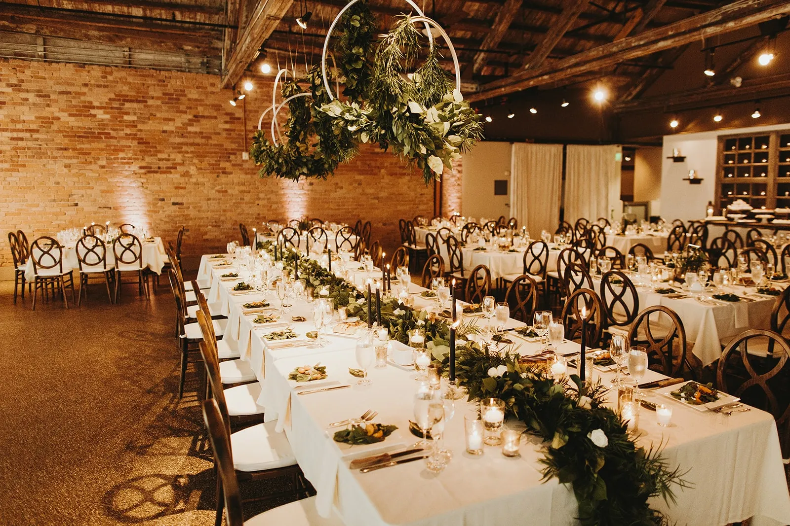 Long tables with a greenery runner, a hanging hoop of foliage above the head of the room