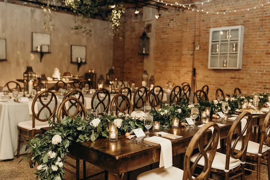 A long wooden table with a greenery and rose runner, brick behind