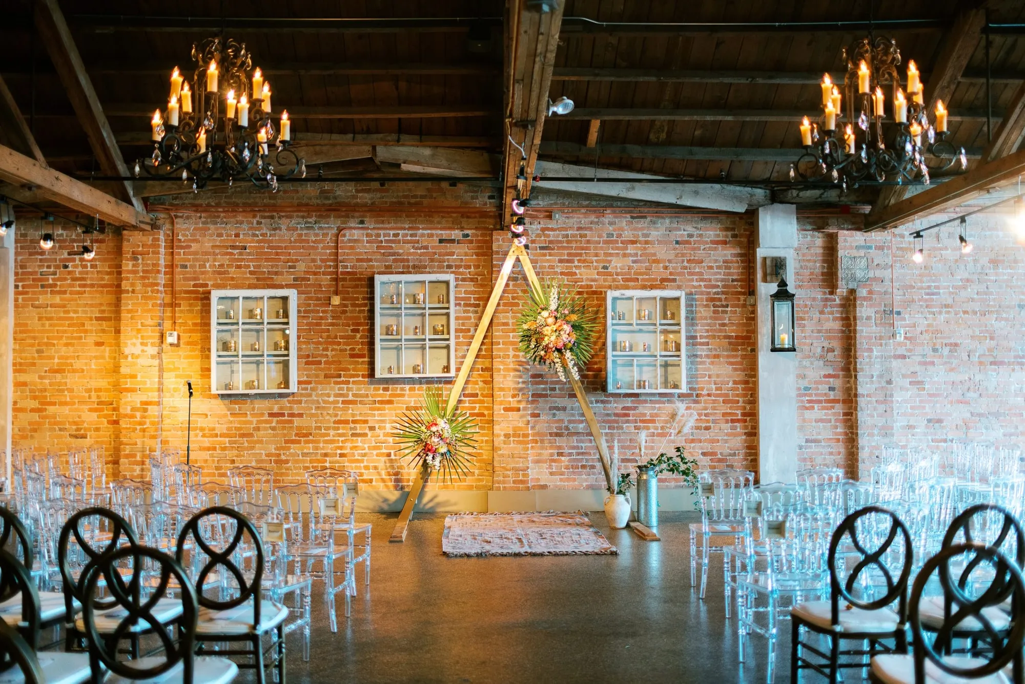 A ceremony set against the brick, a triangular arch and clear chairs in rows