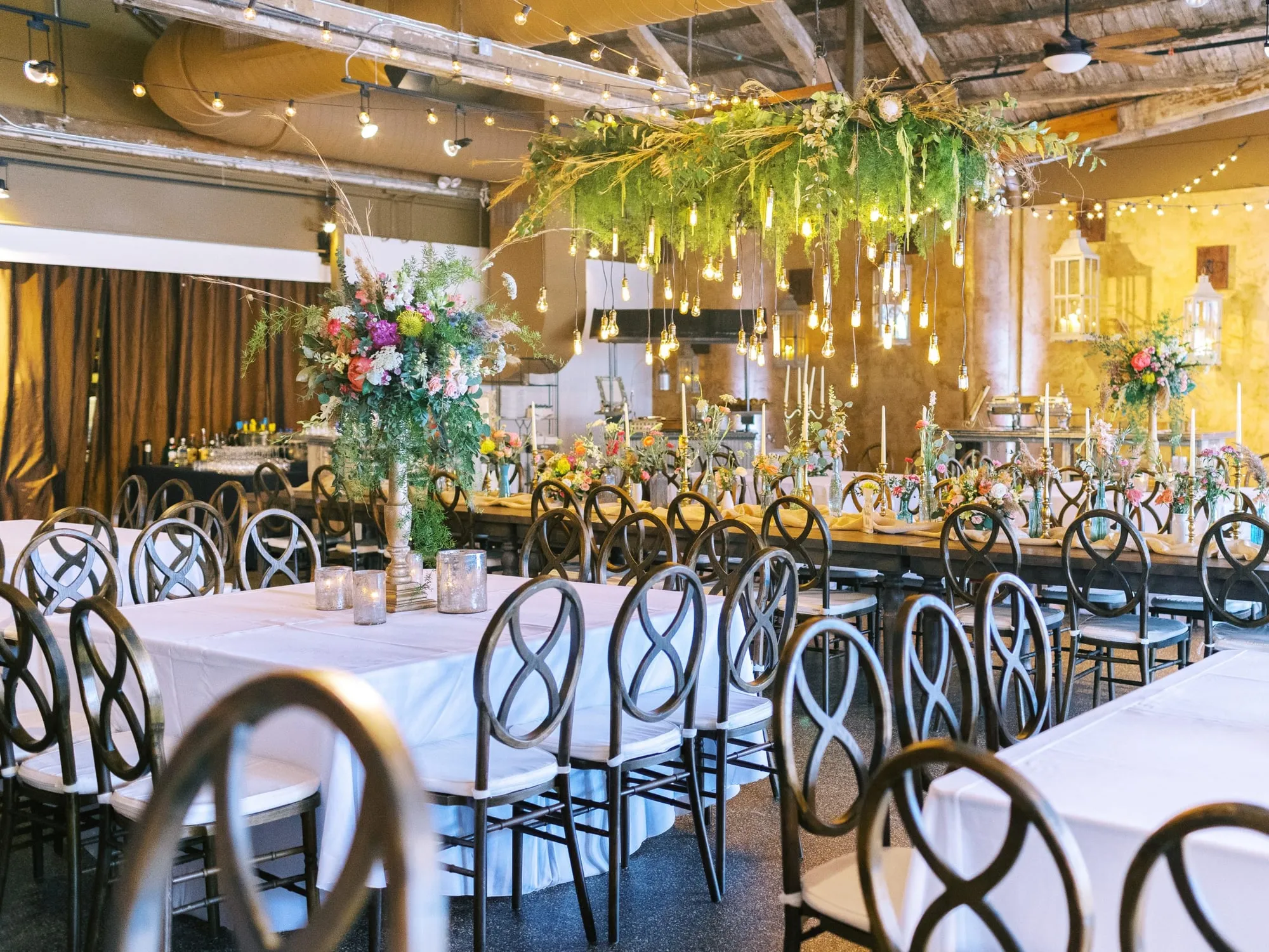 A bright hanging installation of flowers and trailing foliage above a long table