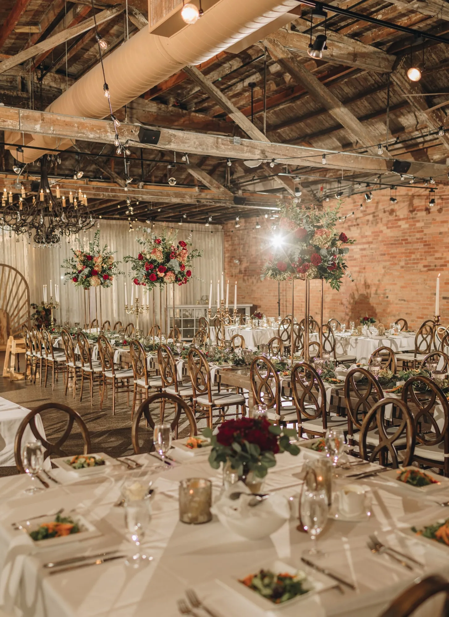Tall floral centerpieces on round tables against the exposed brick