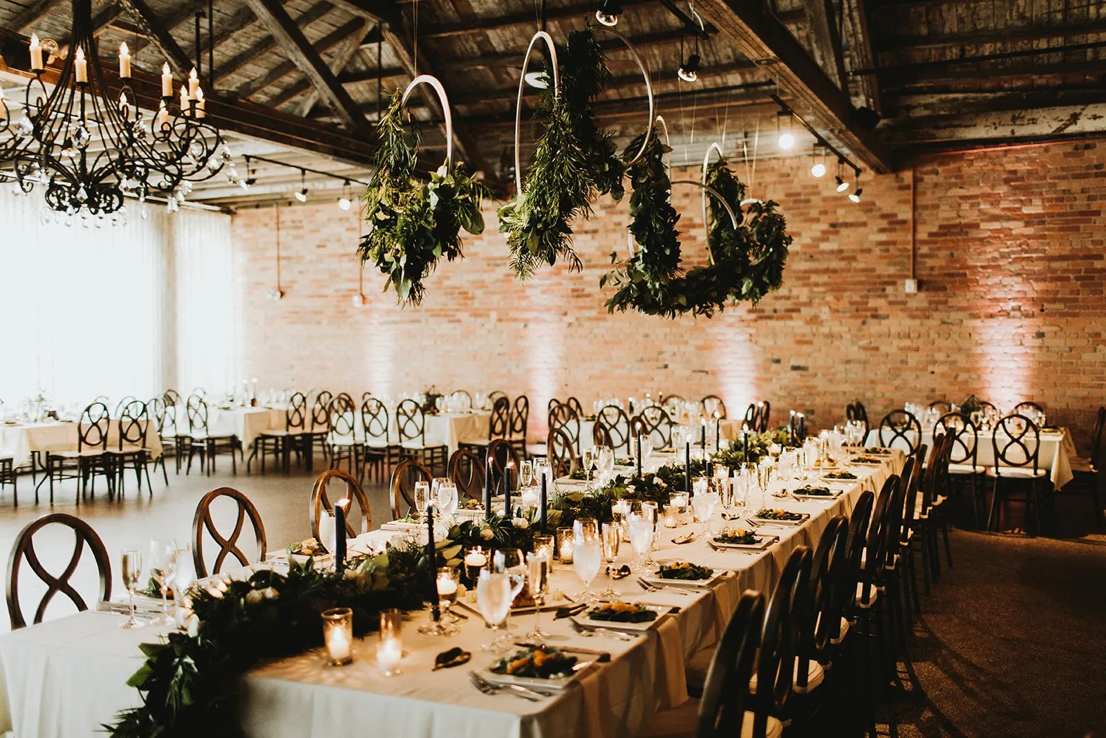 Greenery suspended low over a long table, the room dark around it