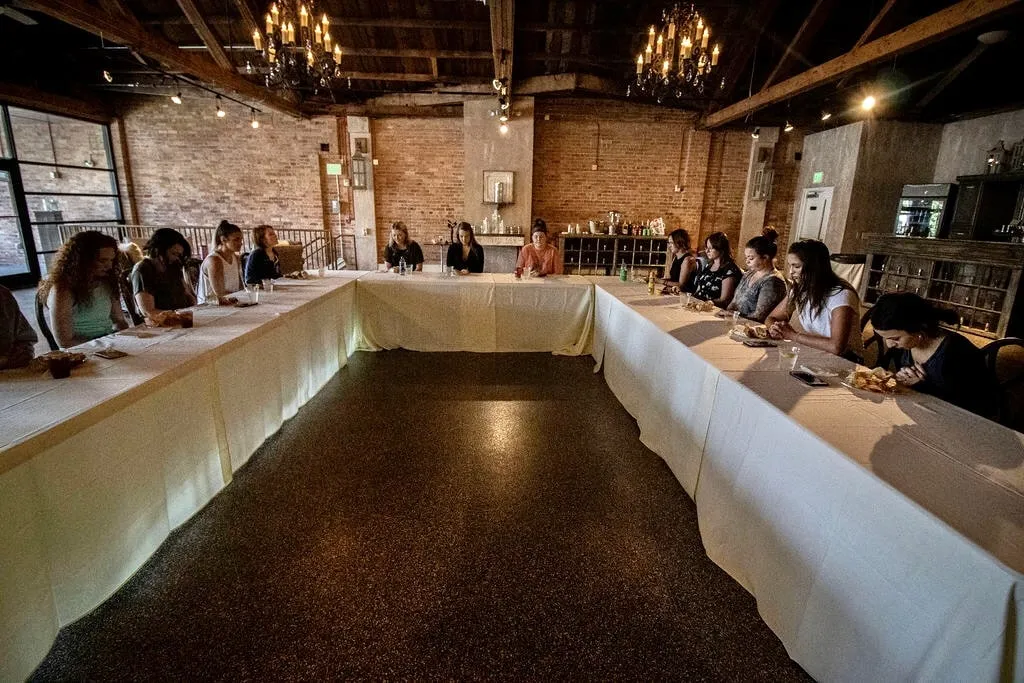 A hollow square of draped tables with attendees seated around the outside, brick behind