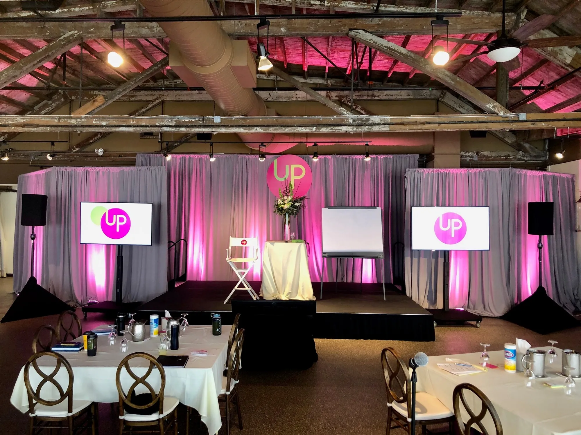 A branded stage with pink uplighting, sponsor screens either side and a lectern