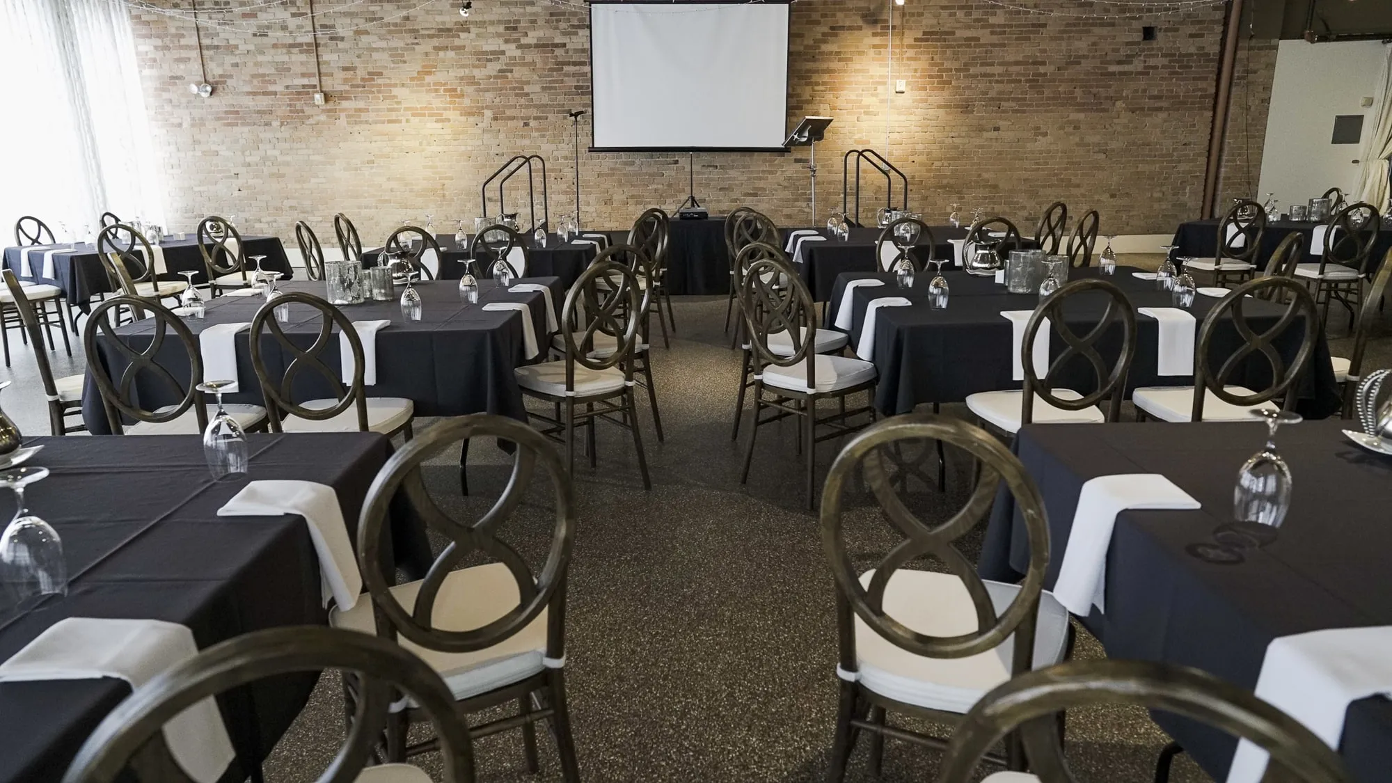 Rounds and rectangles in dark linens facing a projector screen on the brick wall