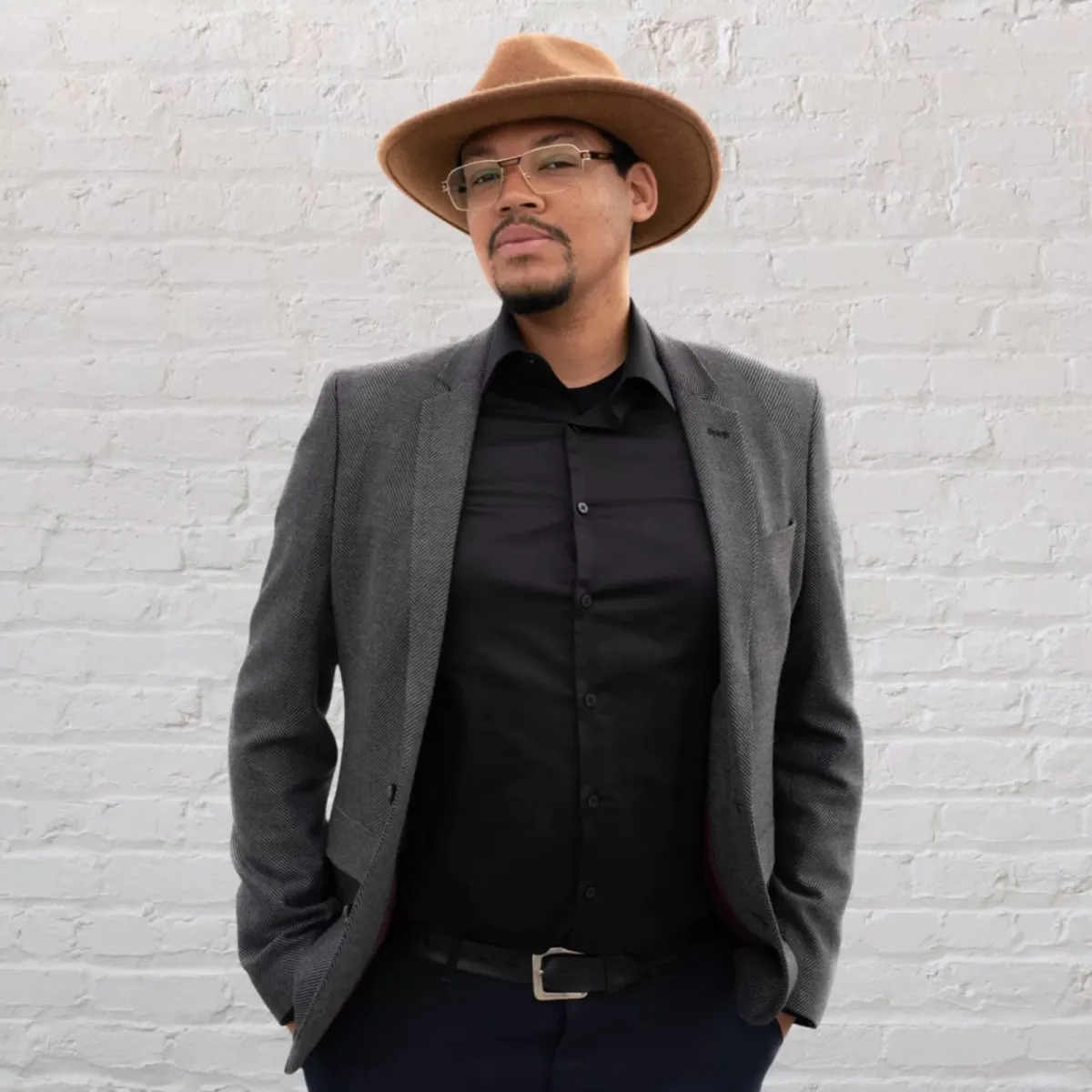 Jason, event manager at The Venue, in a grey jacket and brimmed hat against a white painted brick wall
