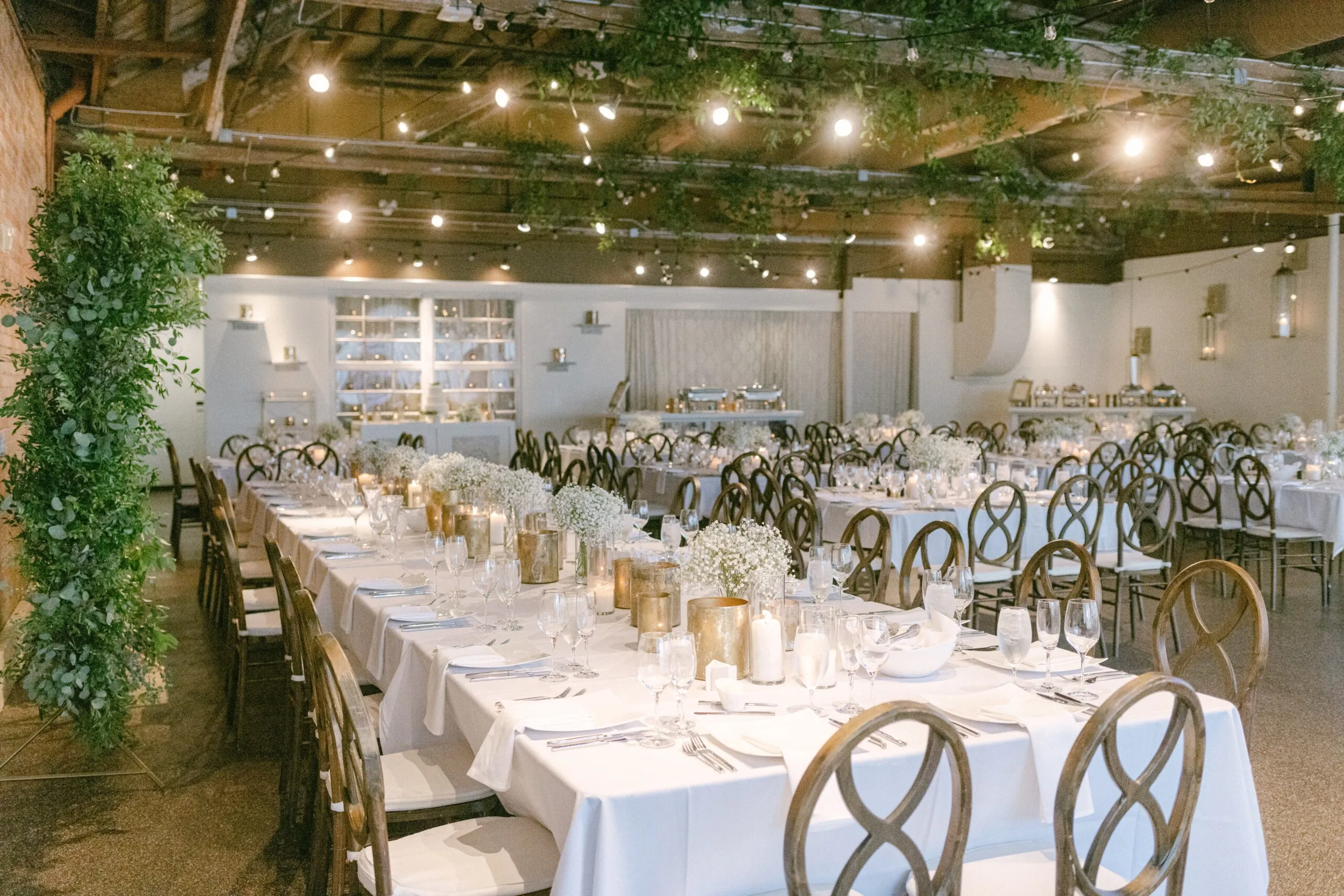 The Market and Mezzanine level arranged for a reception, long tables running beneath suspended greenery and string lights