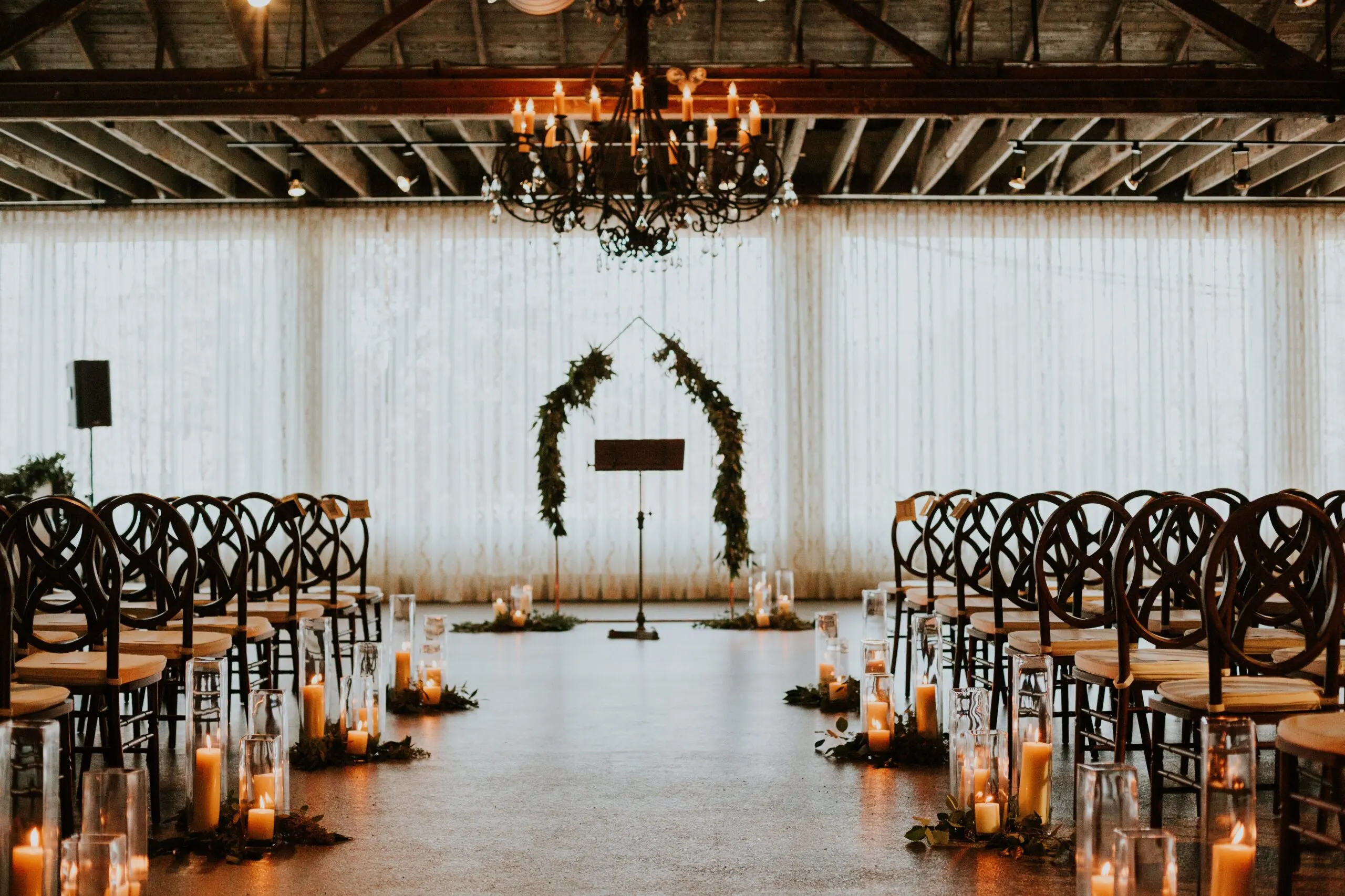 A ceremony set on the Market level, candles lining the aisle beneath a chandelier and exposed roof timbers